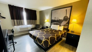 Habitación de hotel con cama, dos mesitas de noche con lámparas, un escritorio, una silla, ventana con cortinas y aire acondicionado.