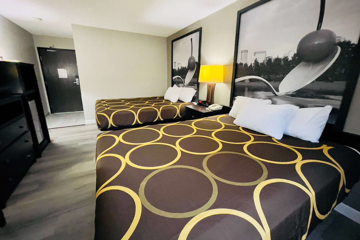 A hotel room with two beds, a desk with a lamp, and a cityscape view.