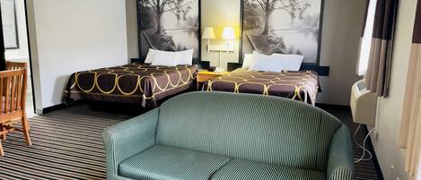 A hotel room with two beds, a sofa, a small table, and a nightstand with a lamp.