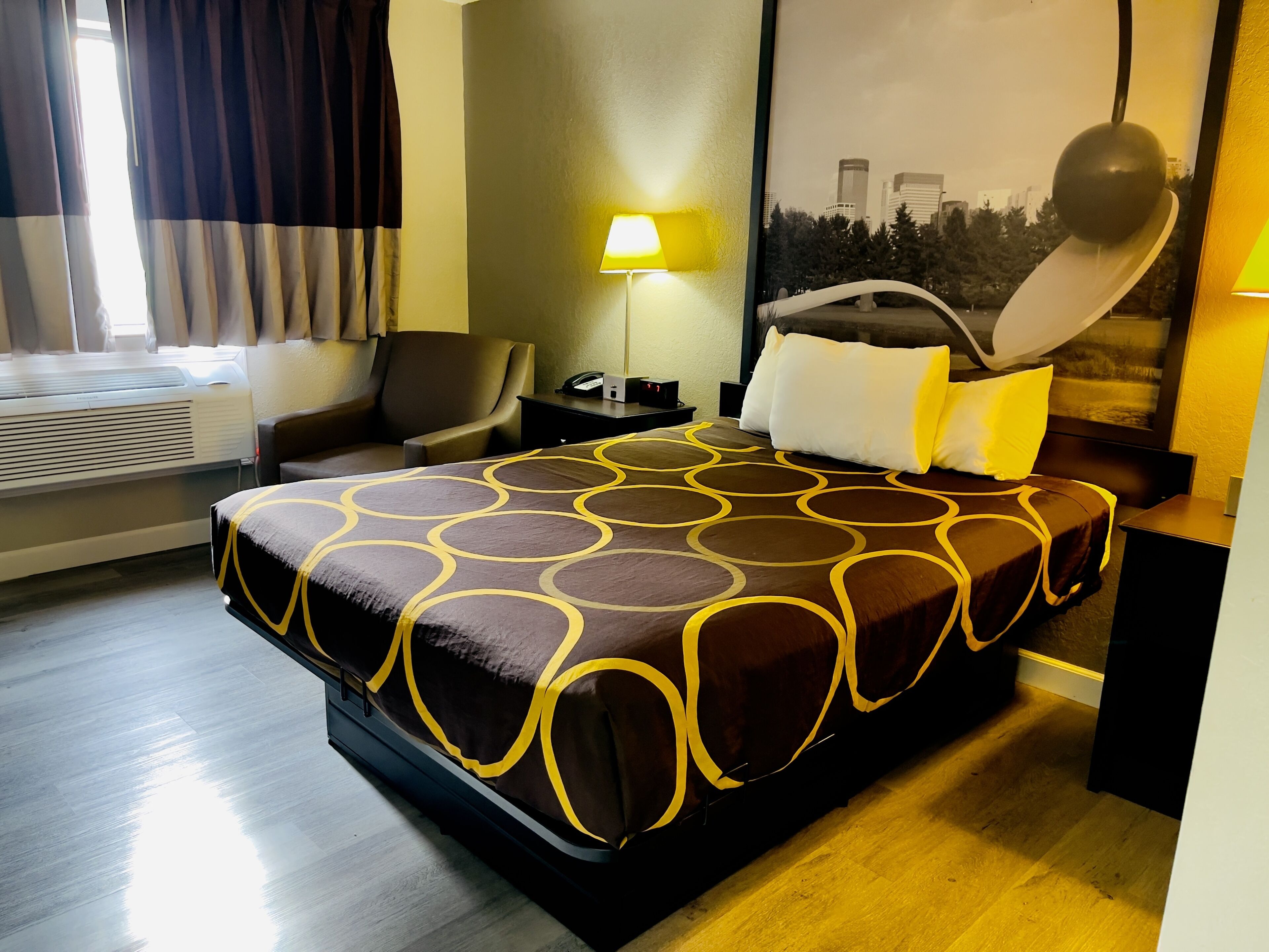 A hotel room with a large bed, a chair, a desk, a lamp, and a window with curtains.