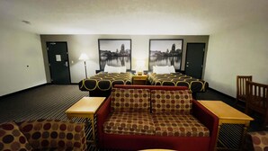 Habitación de hotel con dos camas, un sofá y una silla. Hay dos lámparas en las mesitas de noche.