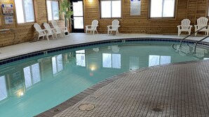 Una piscina interior con paredes de madera, sillas blancas y suelo de baldosas.