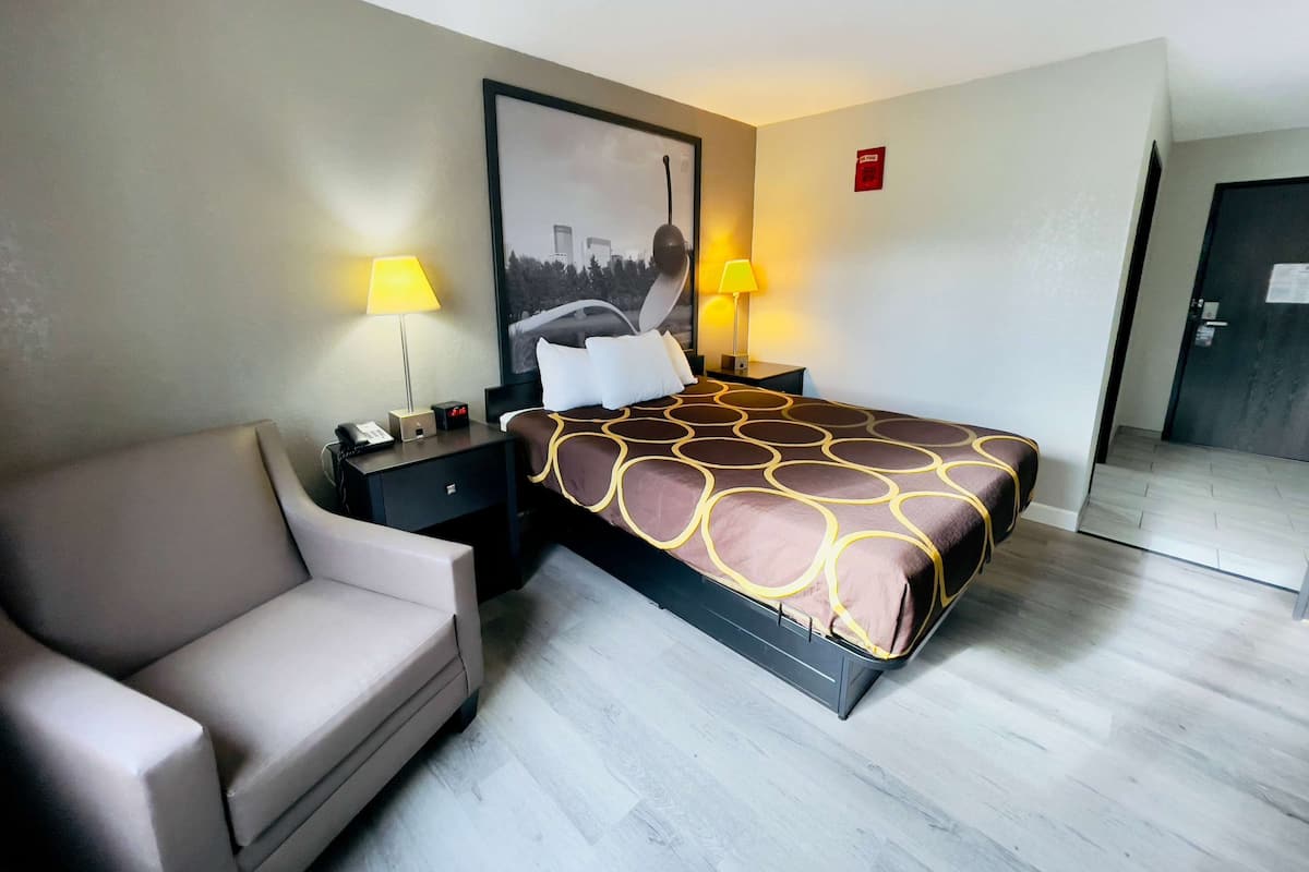 A hotel room with a bed, a sofa, two bedside tables with lamps, a large framed picture on the wall, and a door.