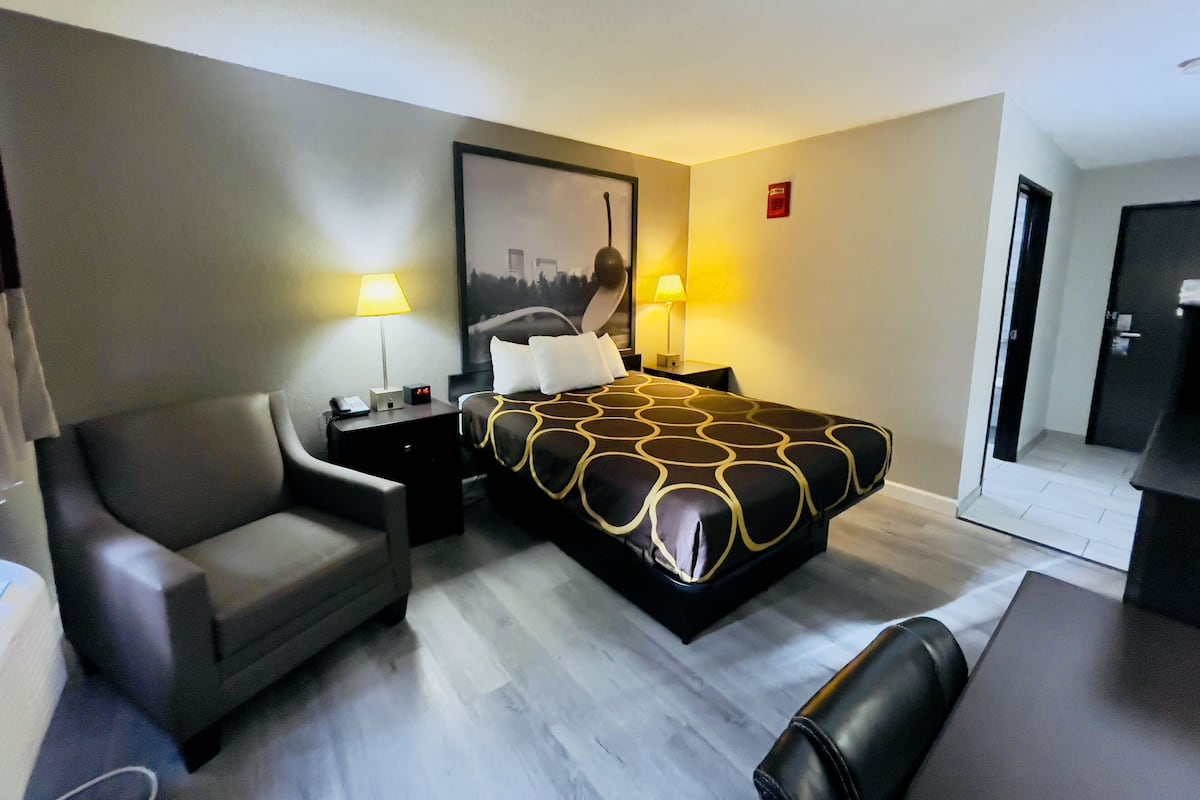 A modern hotel room with a bed, a desk, a chair, and a large window.