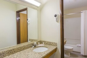 A bathroom with a granite countertop sink, a mirror, a toilet, and a shower curtain.