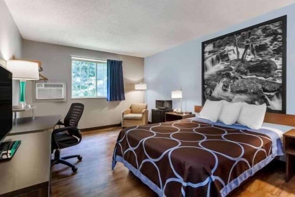 A hotel room with a bed, desk, chair, and a large painting on the wall.