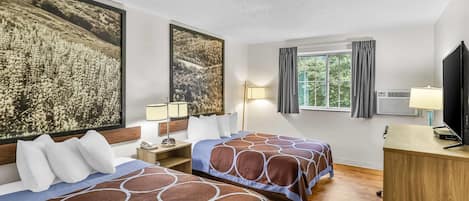 A hotel room with two beds, a desk, a TV, and a window with curtains.