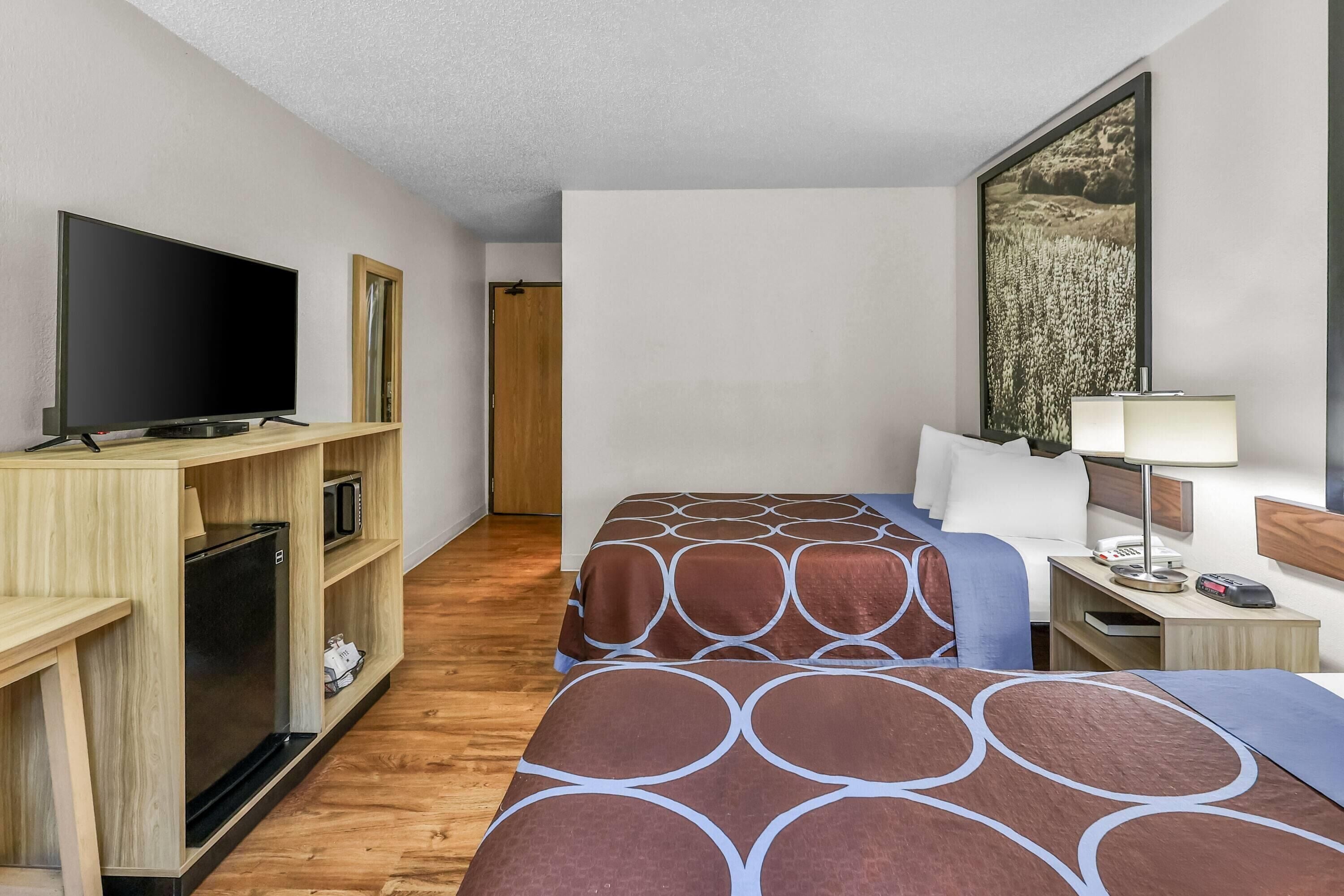 Habitación de hotel con dos camas, televisión, escritorio con lámpara y un cuadro en la pared.