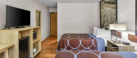 Habitación de hotel con dos camas, televisión, escritorio con lámpara y un cuadro en la pared.