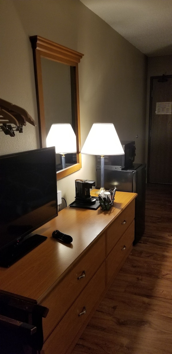 Habitación de hotel con cómoda de madera, televisor de pantalla plana, lámpara y espejo.