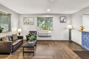 A modern living room with a sofa, a coffee table, a chair, a window with plants, and artwork on the walls.