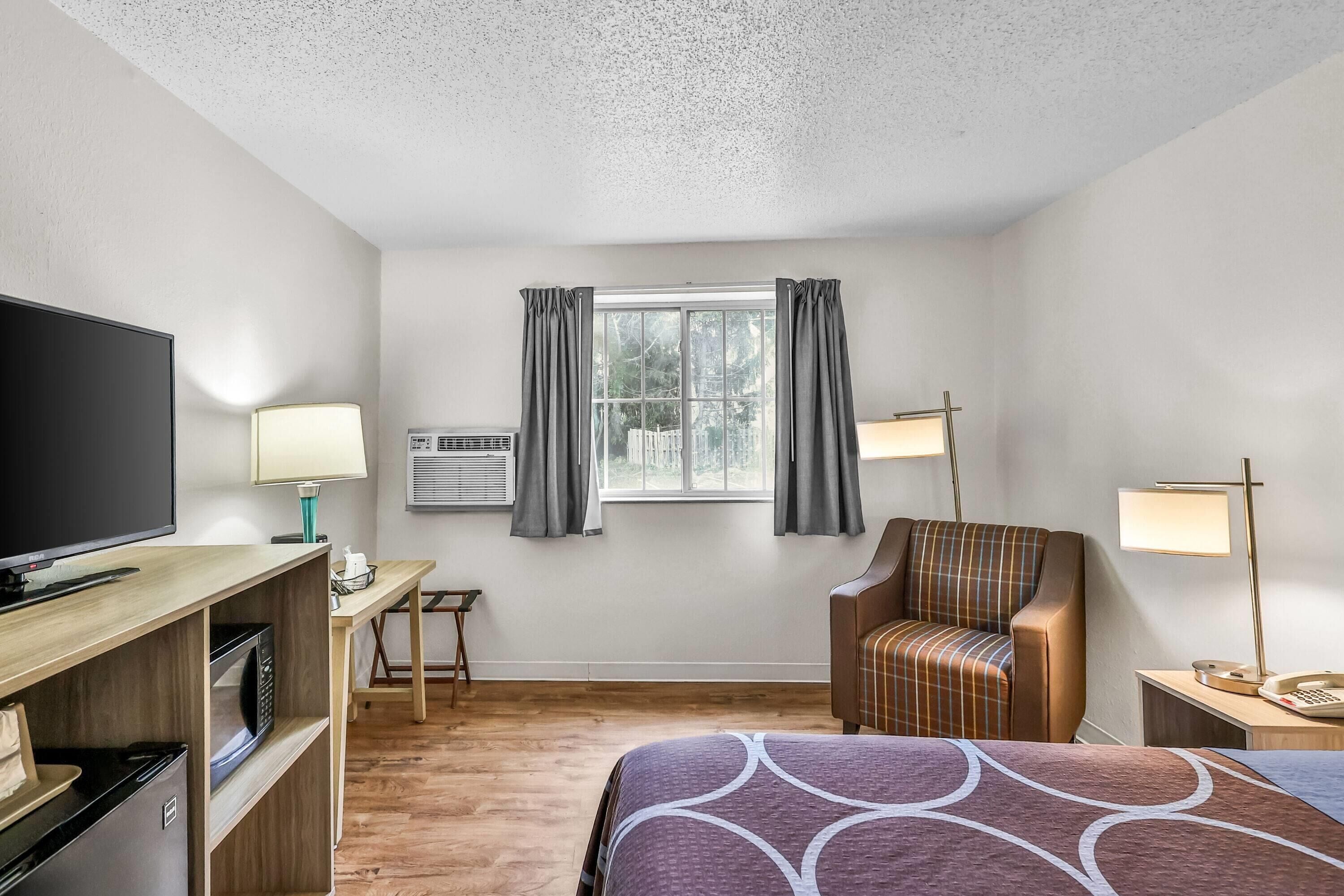 A hotel room with a bed, a TV, a desk, a chair, and a window with curtains.