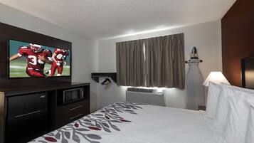 A hotel room with a bed, a flat-screen TV, a microwave, a refrigerator, and a window with curtains.