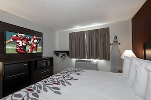 A hotel room with a bed, a flat-screen TV, a microwave, a refrigerator, and a window with curtains. - Red Roof Inn Greensburg (Greensburg)
