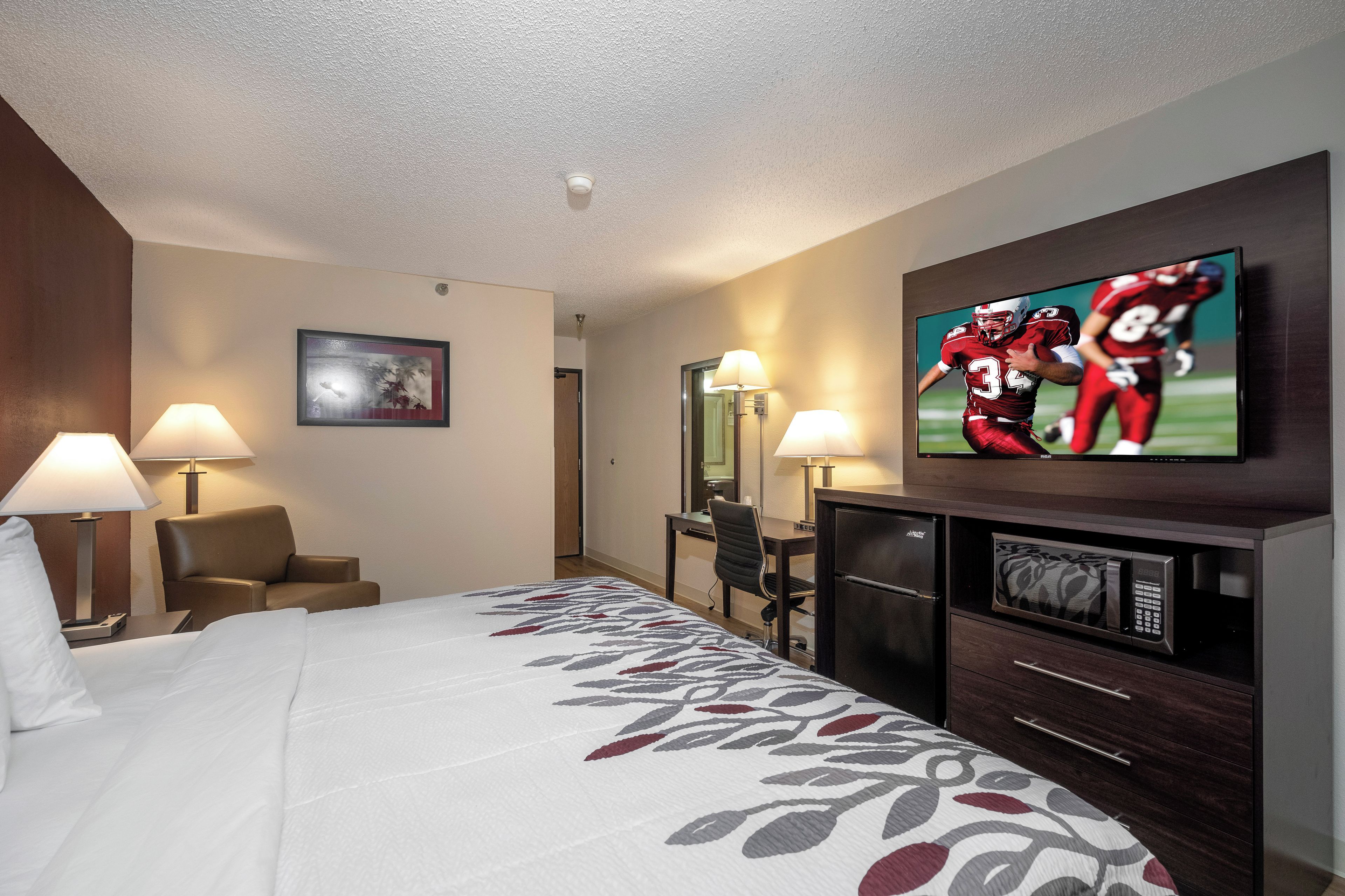 Una habitación de hotel con cama, escritorio, silla, televisor y microondas.