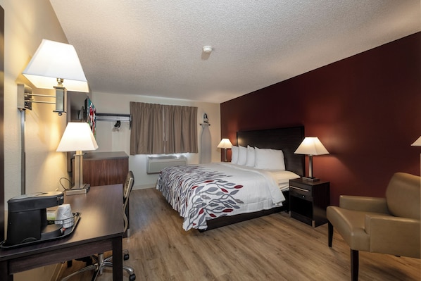 Une chambre d’hôtel avec un lit, des lampes de chevet, un bureau avec un ordinateur, une chaise et une fenêtre avec des rideaux.