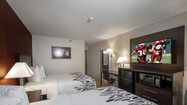 Habitación de hotel con dos camas, un televisor montado en la pared, un escritorio con lámpara y un microondas.