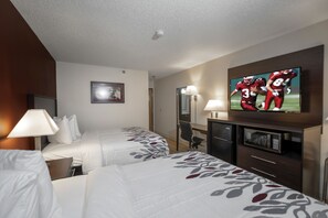 Habitación de hotel con dos camas, un televisor montado en la pared, un escritorio con lámpara y un microondas.