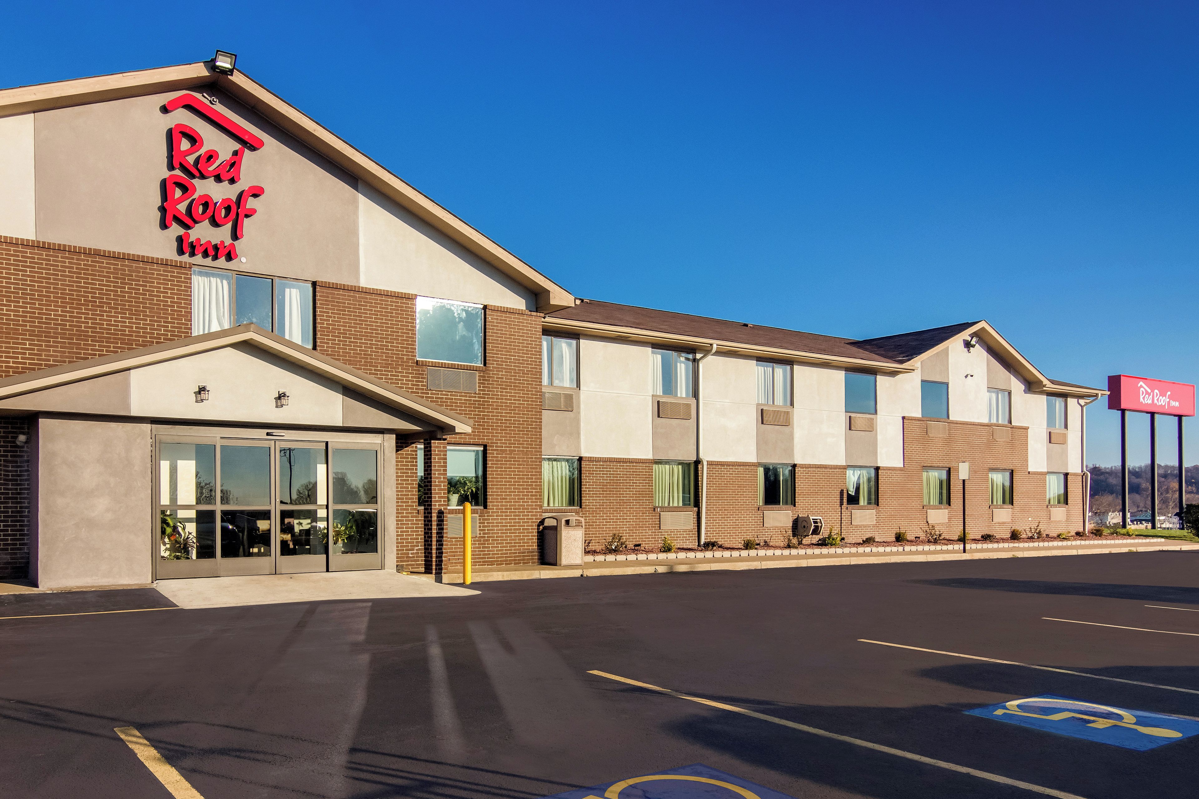 Een Red Roof Inn met een gevel van baksteen, grote ramen en een parkeerplaats met mindervalidenparkeerplaatsen.