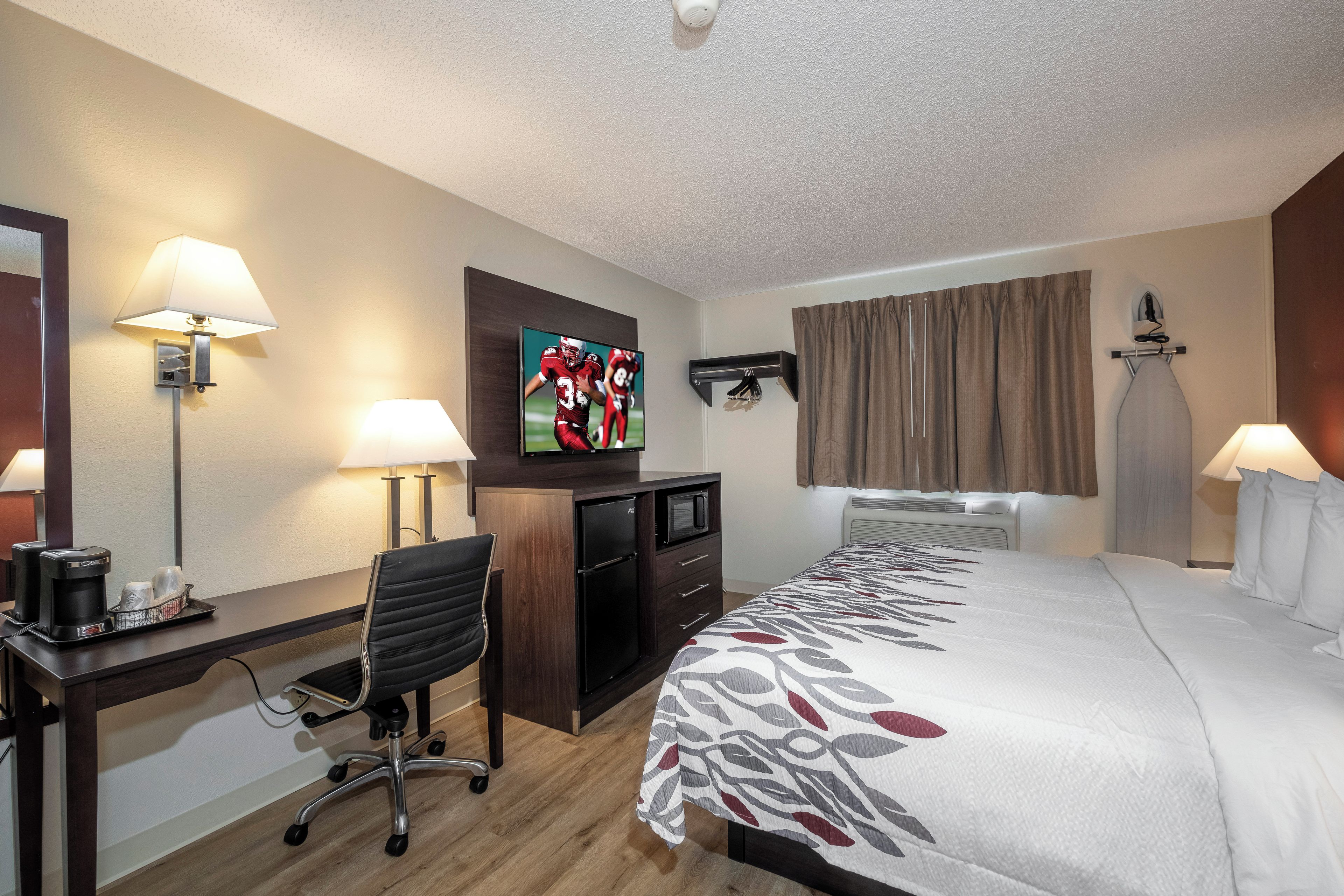 A hotel room with a bed, desk, chair, television, and a wall-mounted ironing board.
