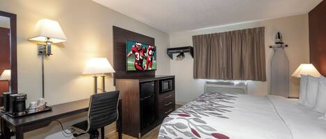 A hotel room with a bed, desk, chair, television, and a wall-mounted ironing board.