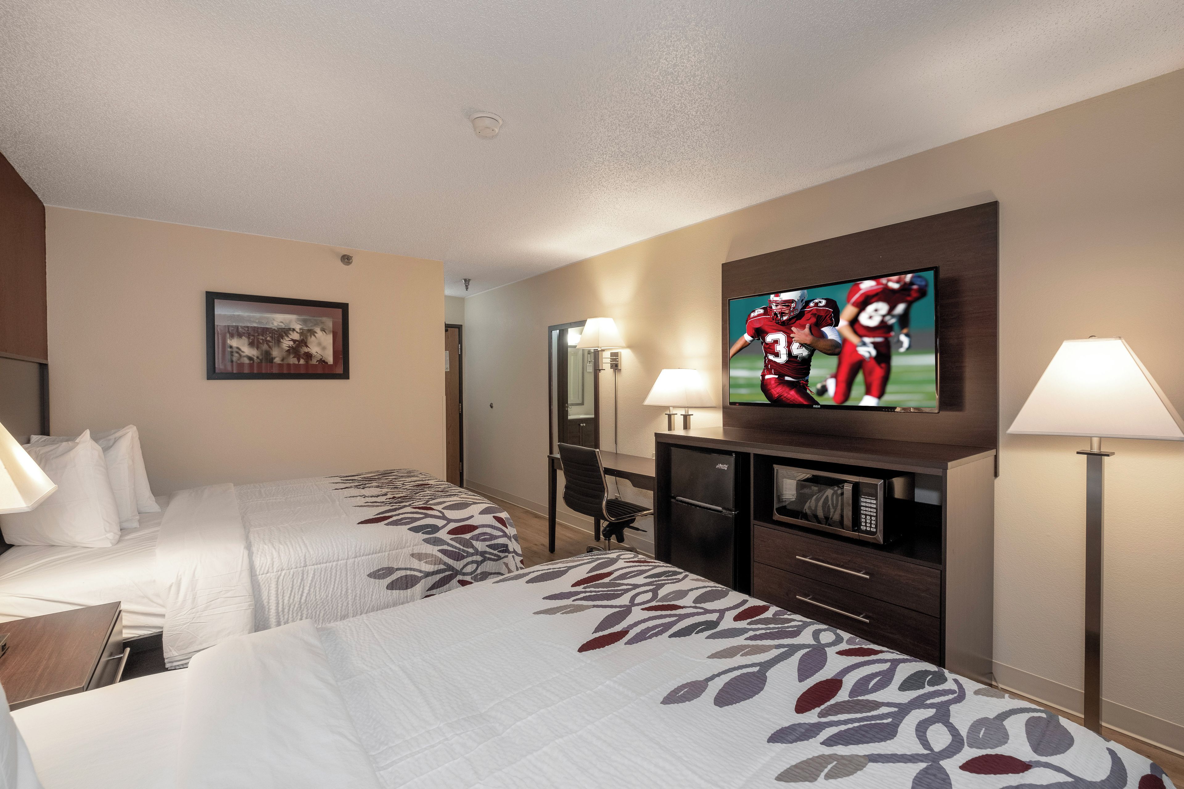A hotel room with two beds, a television, a desk, a chair, and a minibar.