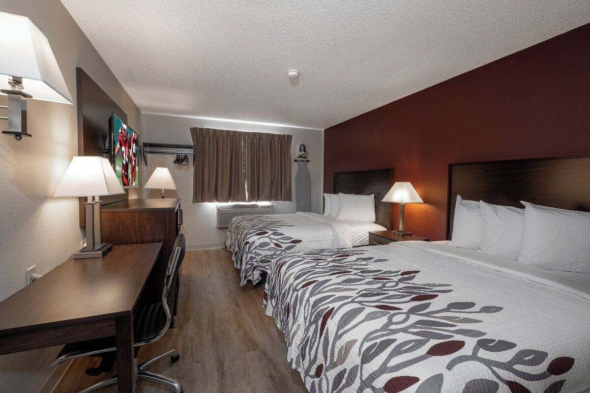 Habitación de hotel con una cama grande, dos mesitas de noche con lámparas, un escritorio con una silla, un armario y un ventanal con cortinas.