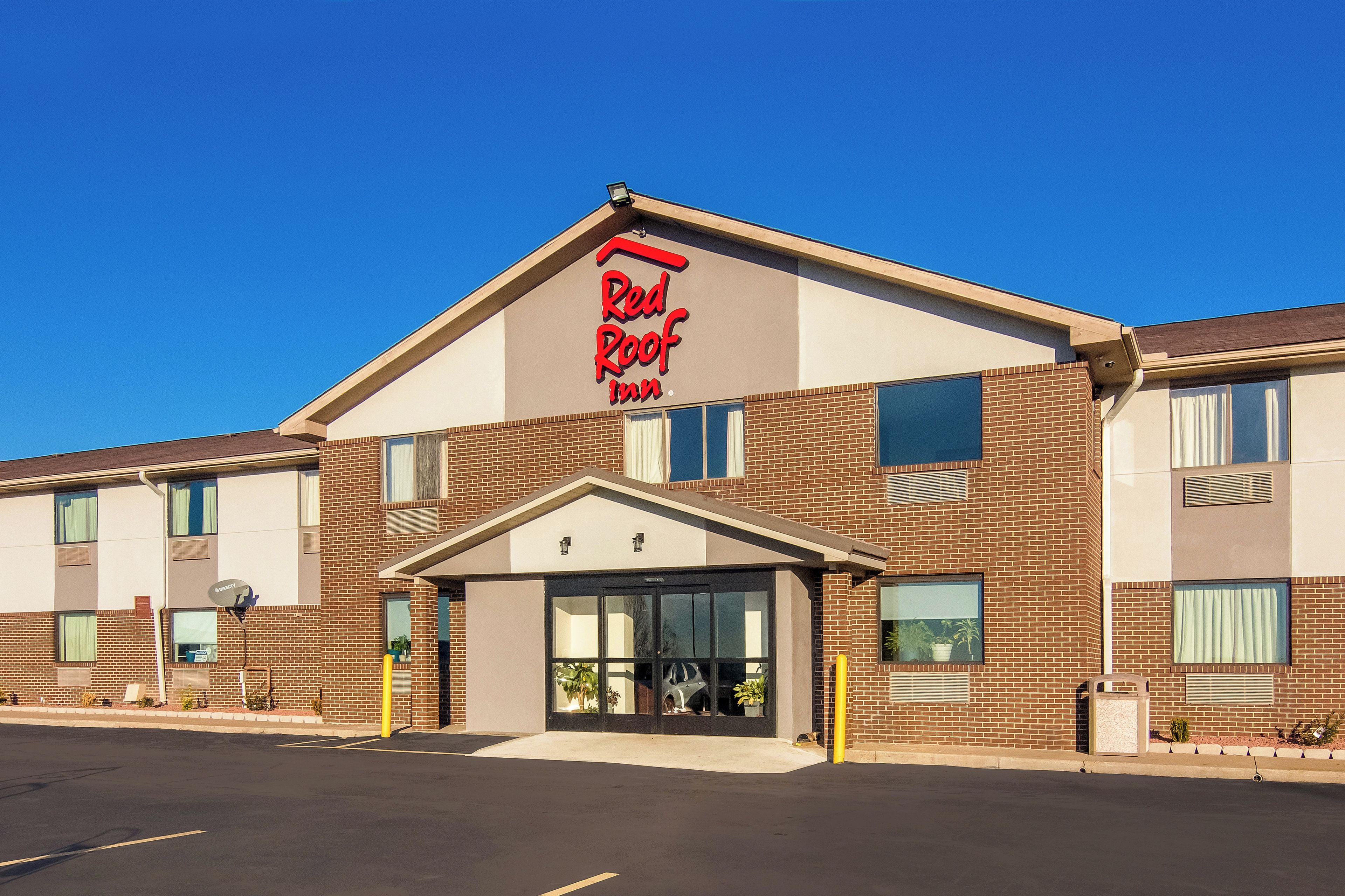 A Red Roof Inn with a brick facade, large windows, and a clear blue sky.