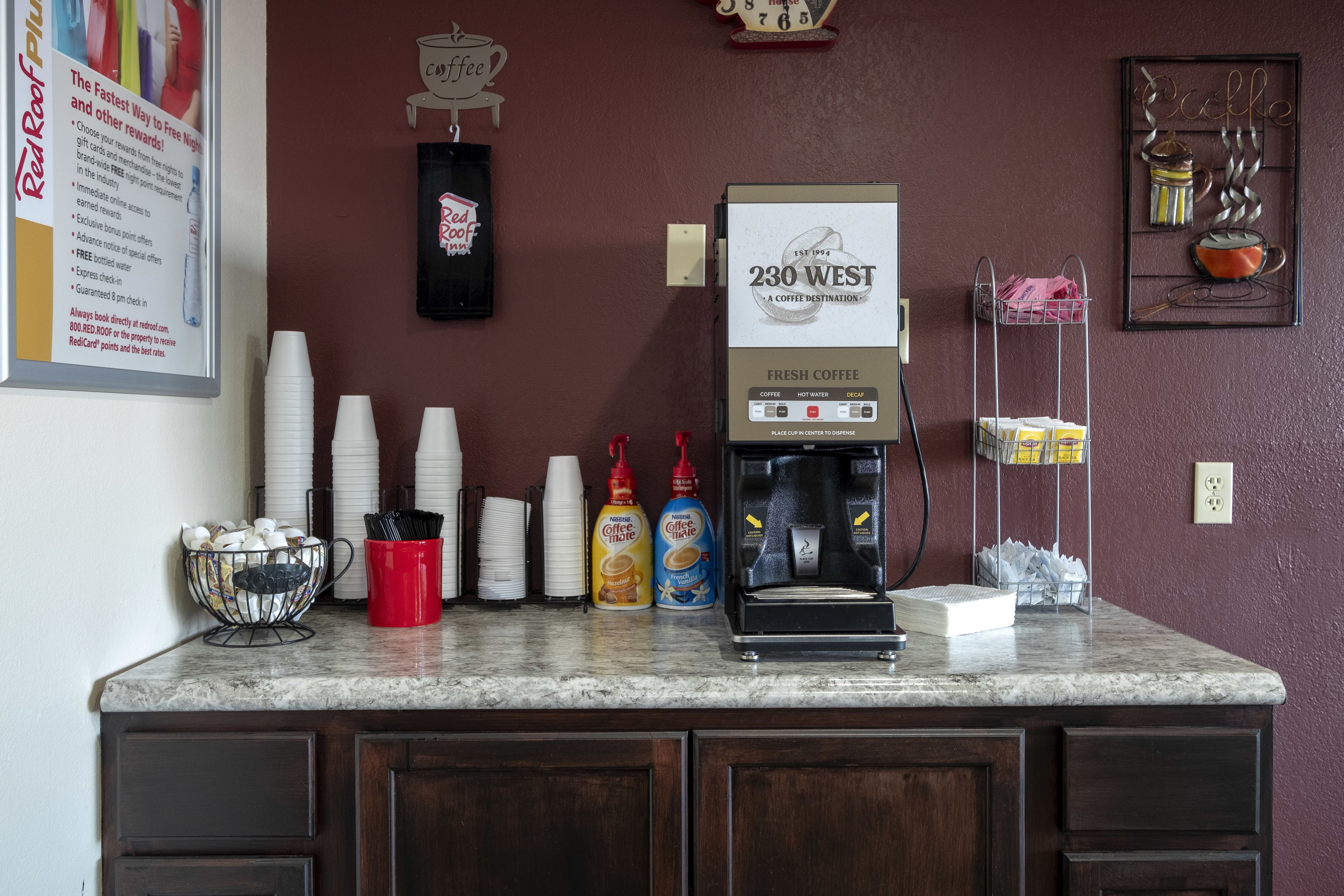A coffee station with a coffee machine, cups, and condiment dispensers.