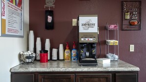 Una estación de café con una máquina de café, tazas y dispensadores de condimentos.