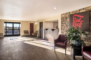 Un vestíbulo de hotel con una recepción, zona de estar y vistas a través de puertas de cristal.