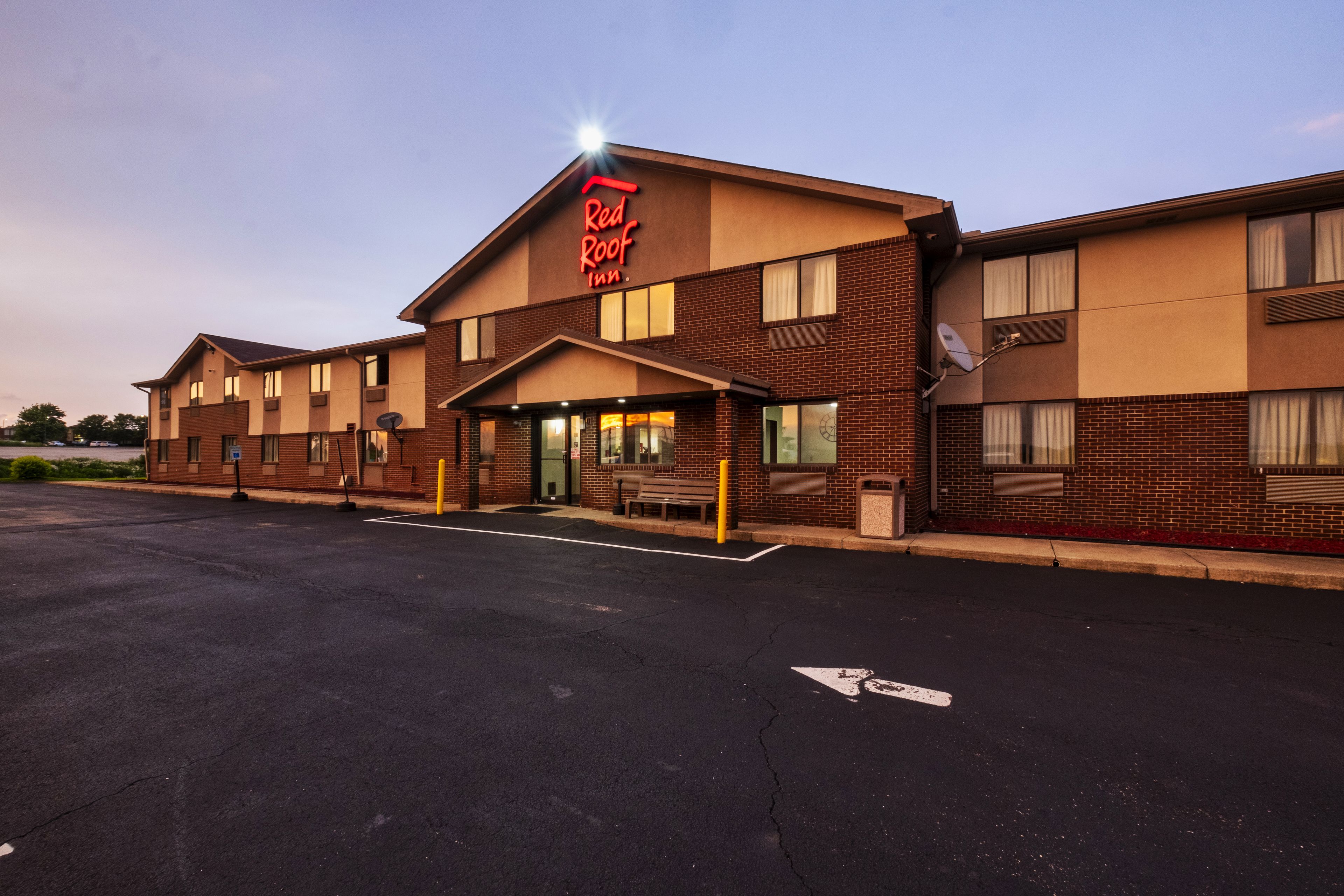 A Red Roof Inn with a brick facade, a parking lot, and a clear sky.