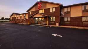 Un Red Roof Inn con fachada de ladrillo, estacionamiento y cielo despejado.