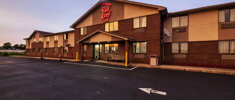 A Red Roof Inn with a brick facade, a parking lot, and a clear sky.