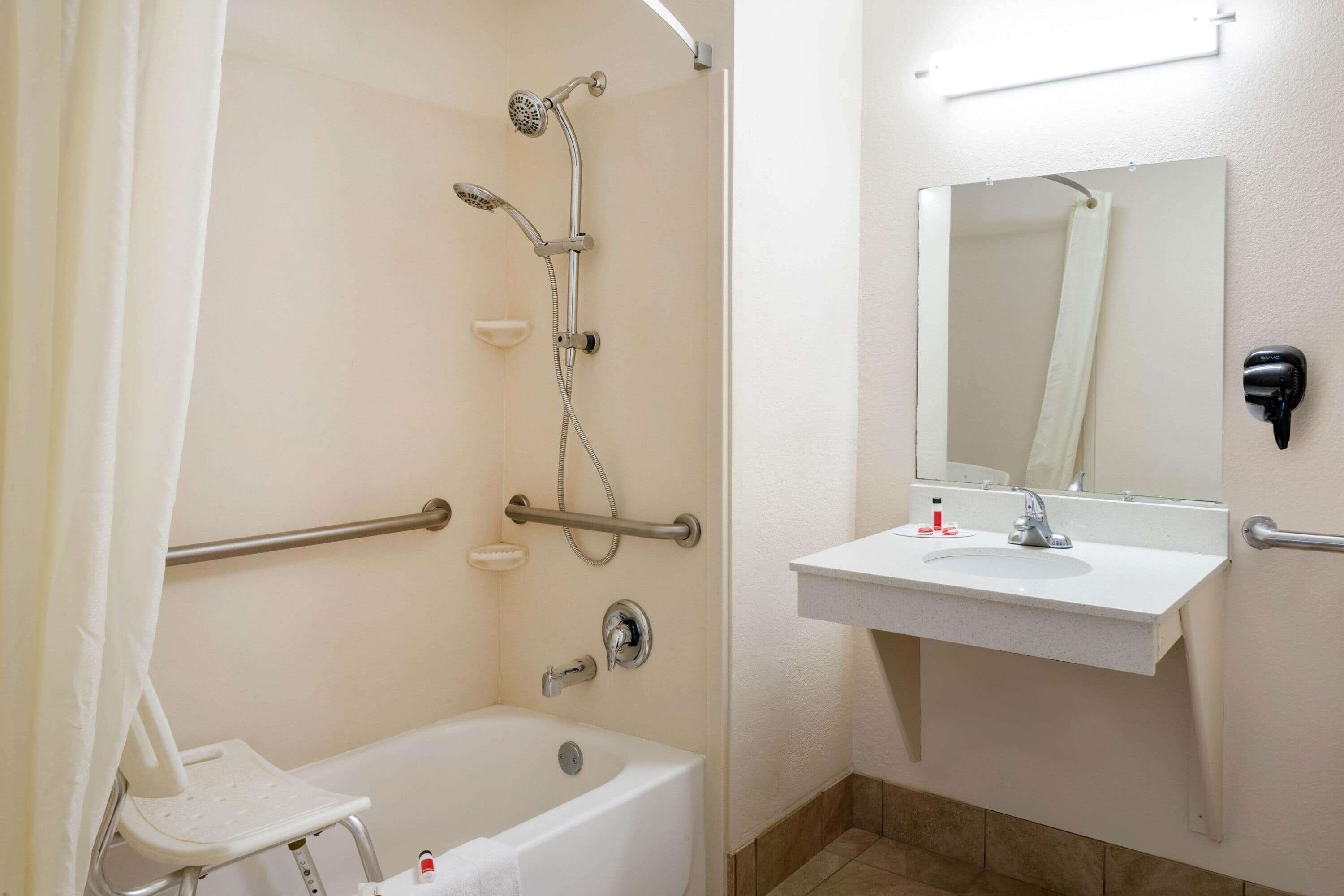 Een badkamer met een badkuip, douche, handdroger en spiegel.