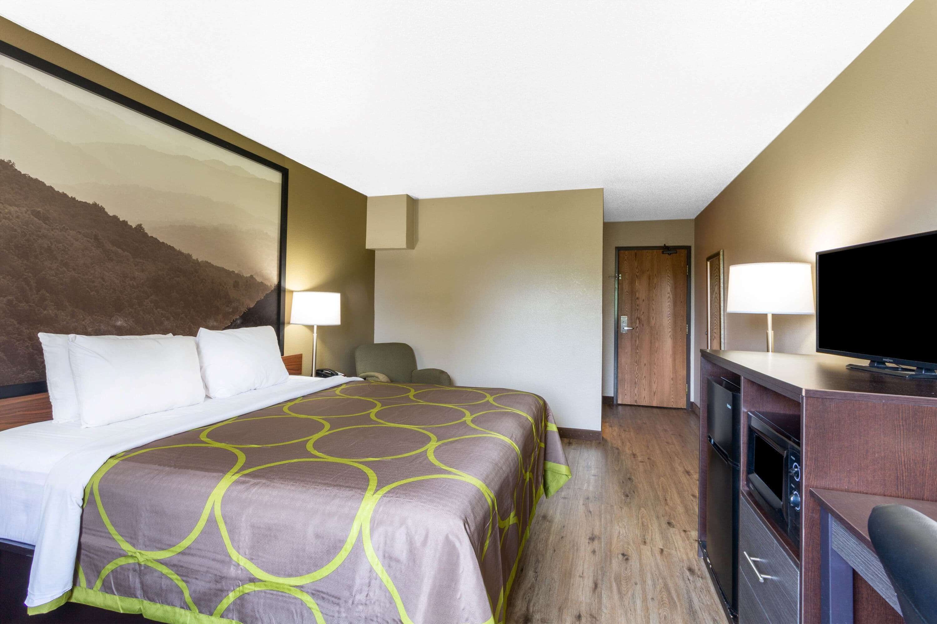 A hotel room with a bed, a desk, a television, and a door.
