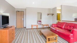 Une chambre d’hôtel avec un téléviseur posé sur un meuble en bois, un canapé en cuir rouge, une table basse en bois et un tapis à rayures.