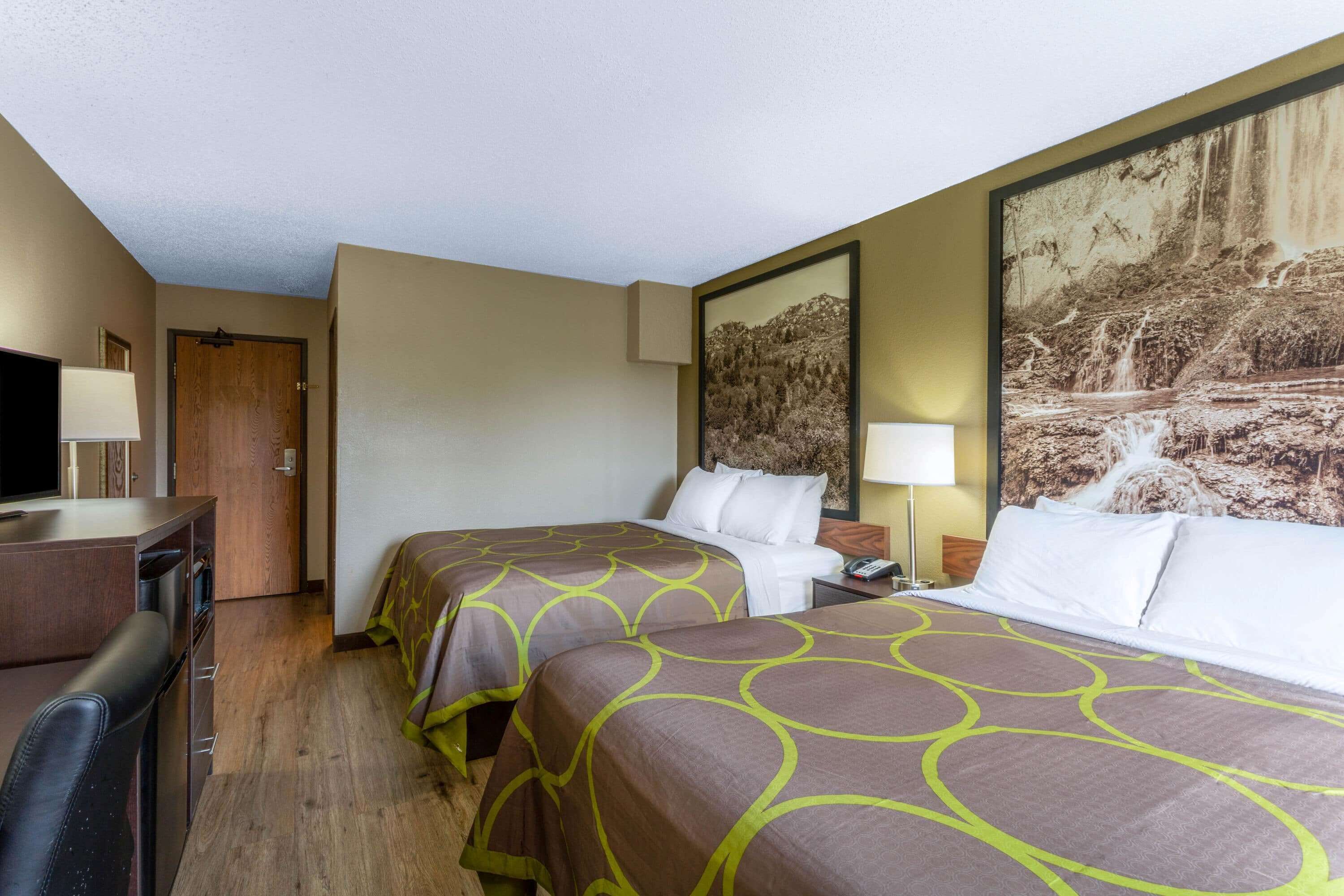 Habitación de hotel con dos camas, un escritorio, un televisor y un cuadro grande con una cascada.