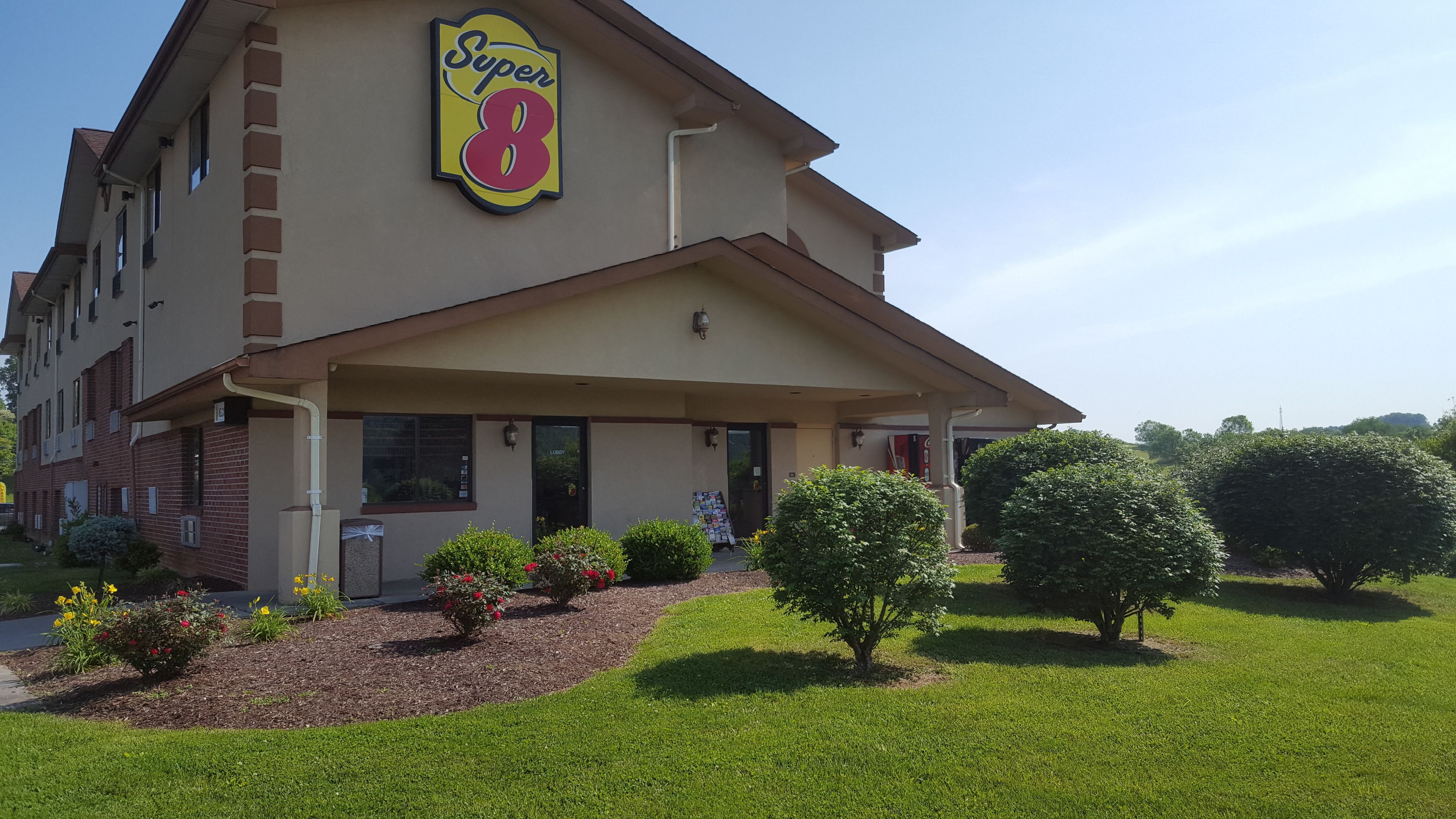 A hotel with a 'Super 8' sign, a covered entrance, and a well-maintained lawn with shrubs and flowers.