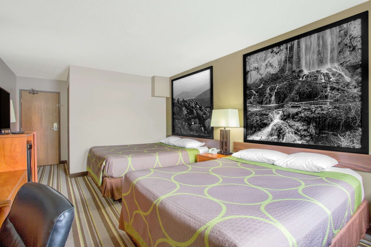 A hotel room with two beds, a desk, a chair, and a large waterfall painting on the wall.