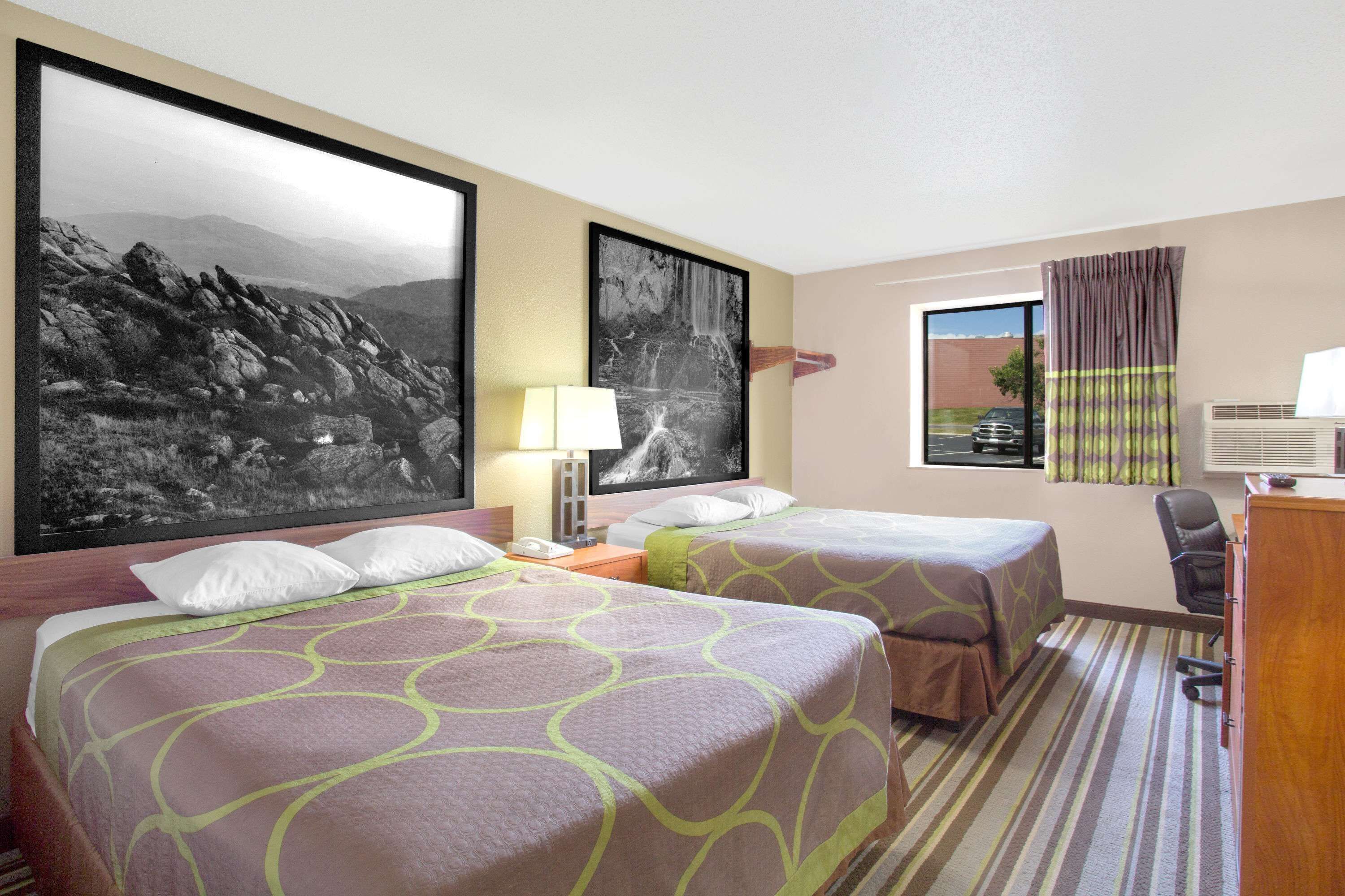 A hotel room with two beds, a desk, a chair, and large framed pictures on the walls.