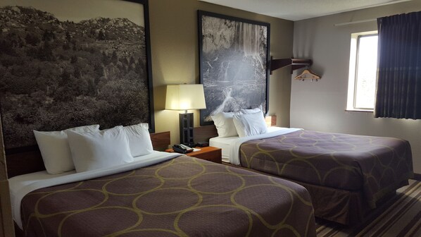 A hotel room with two beds, a large painting of a waterfall, a nightstand with a lamp, and a window with curtains.