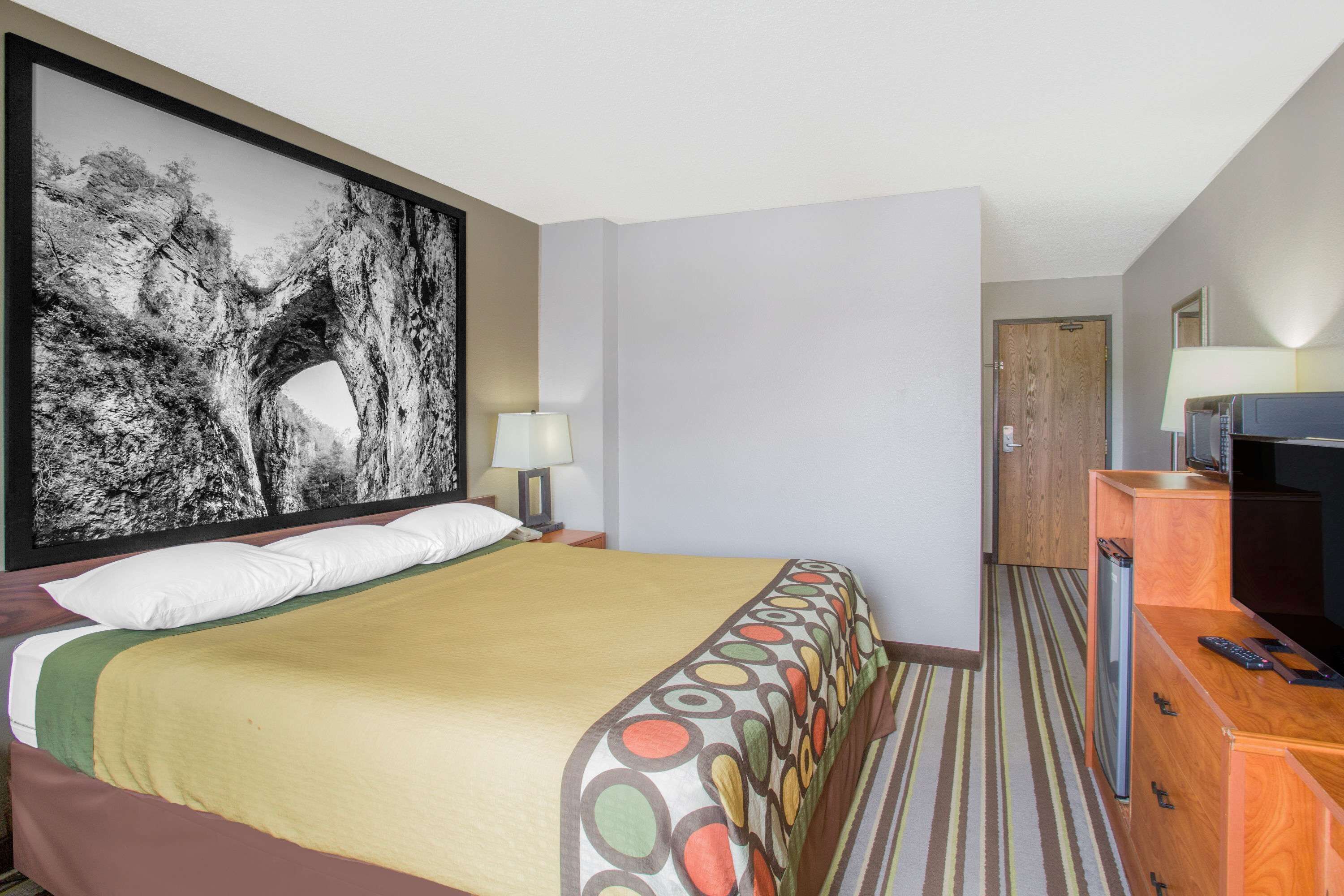 Una habitació d'hotel amb un llit gran, una televisió, un escriptori amb un ordinador i un quadre a la paret.
