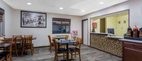 A dining area with wooden chairs and a table, a framed picture on the wall, and a counter with a mirror.