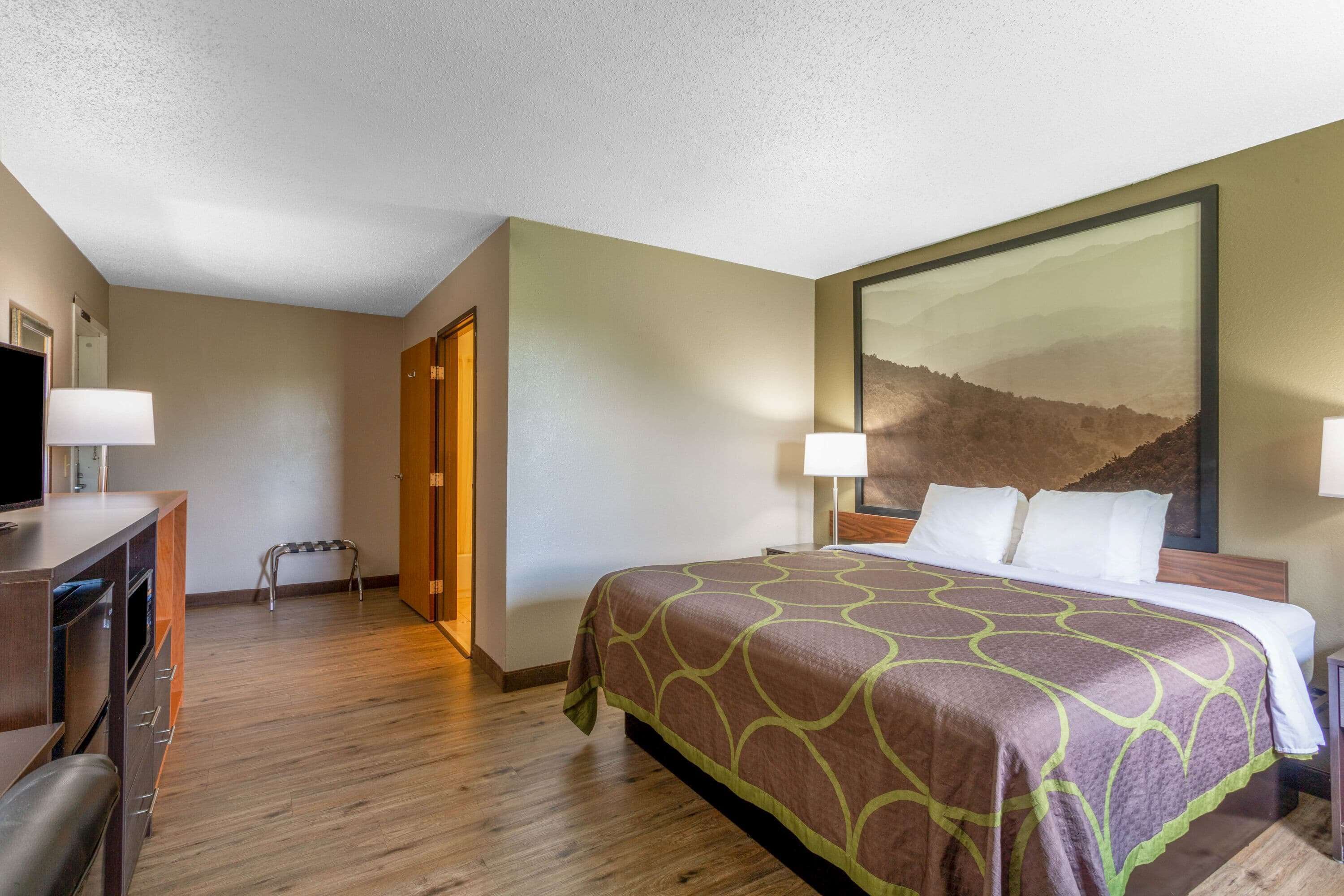 Una habitación de hotel con una cama, un escritorio con lámpara, un televisor y una puerta.