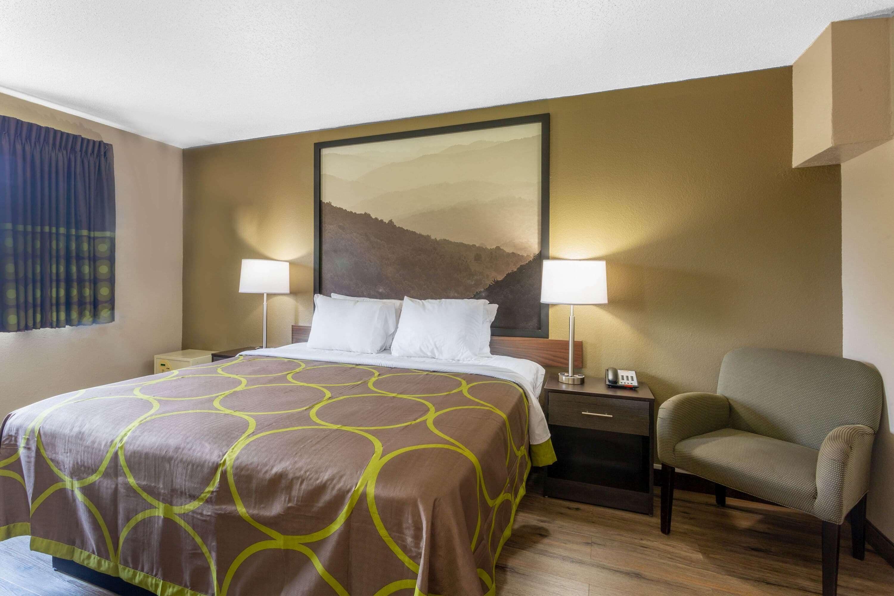 A hotel room with a large bed, two bedside lamps, a chair, a nightstand, and a painting on the wall.