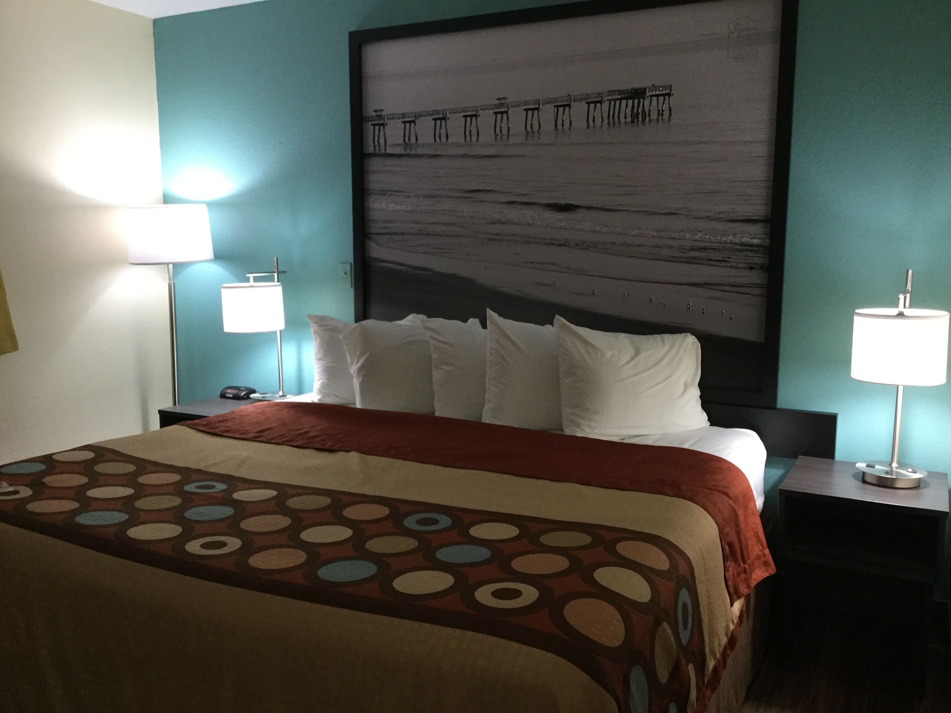 Ein Hotelzimmer mit Bett, zwei Nachttischlampen, einem großen abstrakten Gemälde an der Wand und einer gemusterten Tagesdecke.