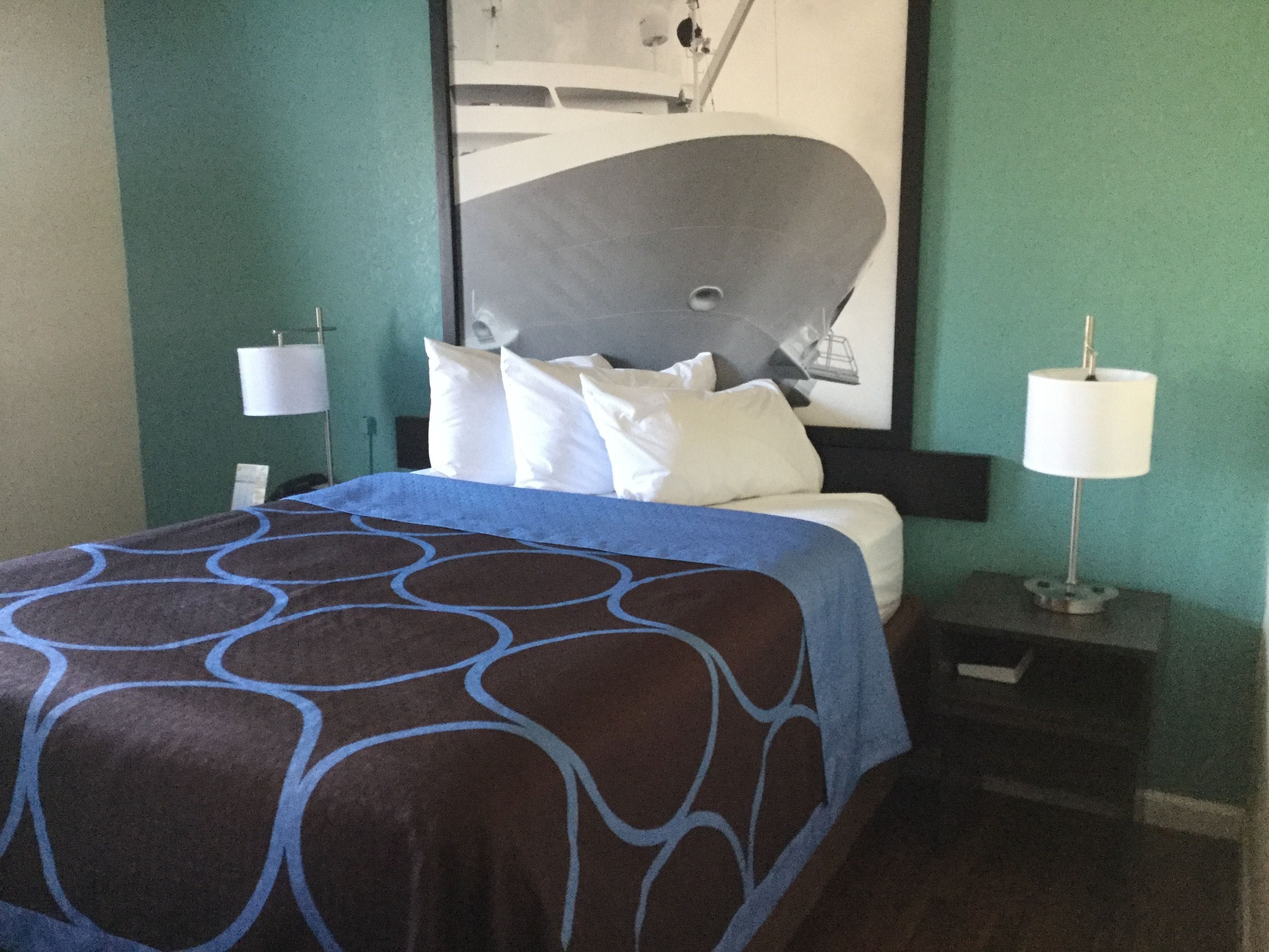 A hotel room with a bed, a nightstand, a lamp, and a large abstract painting on the wall.