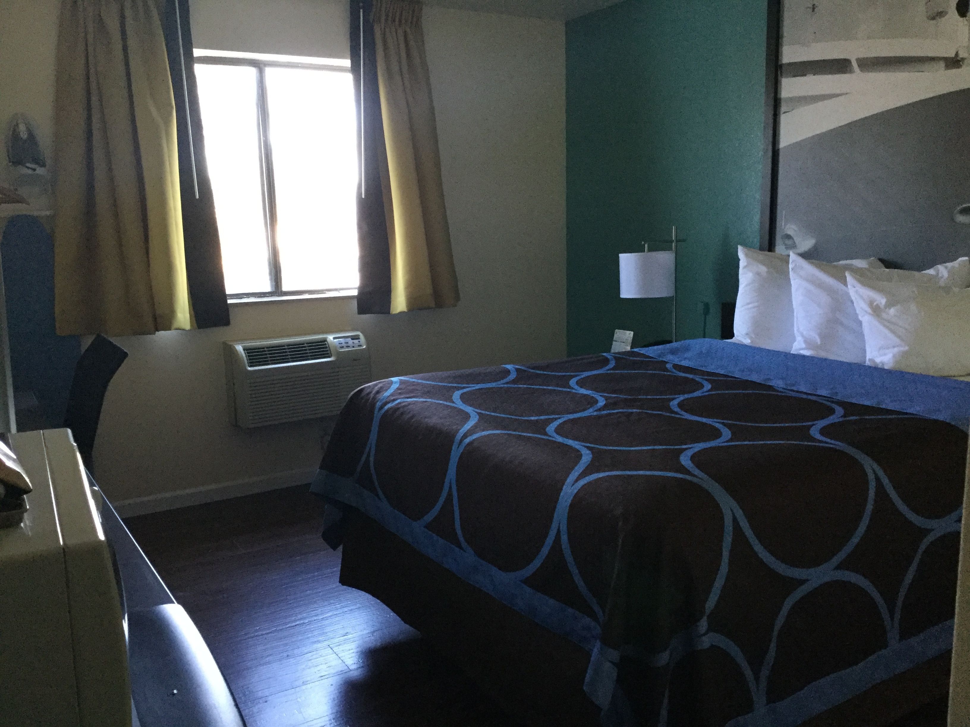 A hotel room with a bed, a desk, an air conditioner, and curtains.