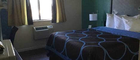 A hotel room with a bed, a desk, an air conditioner, and curtains.